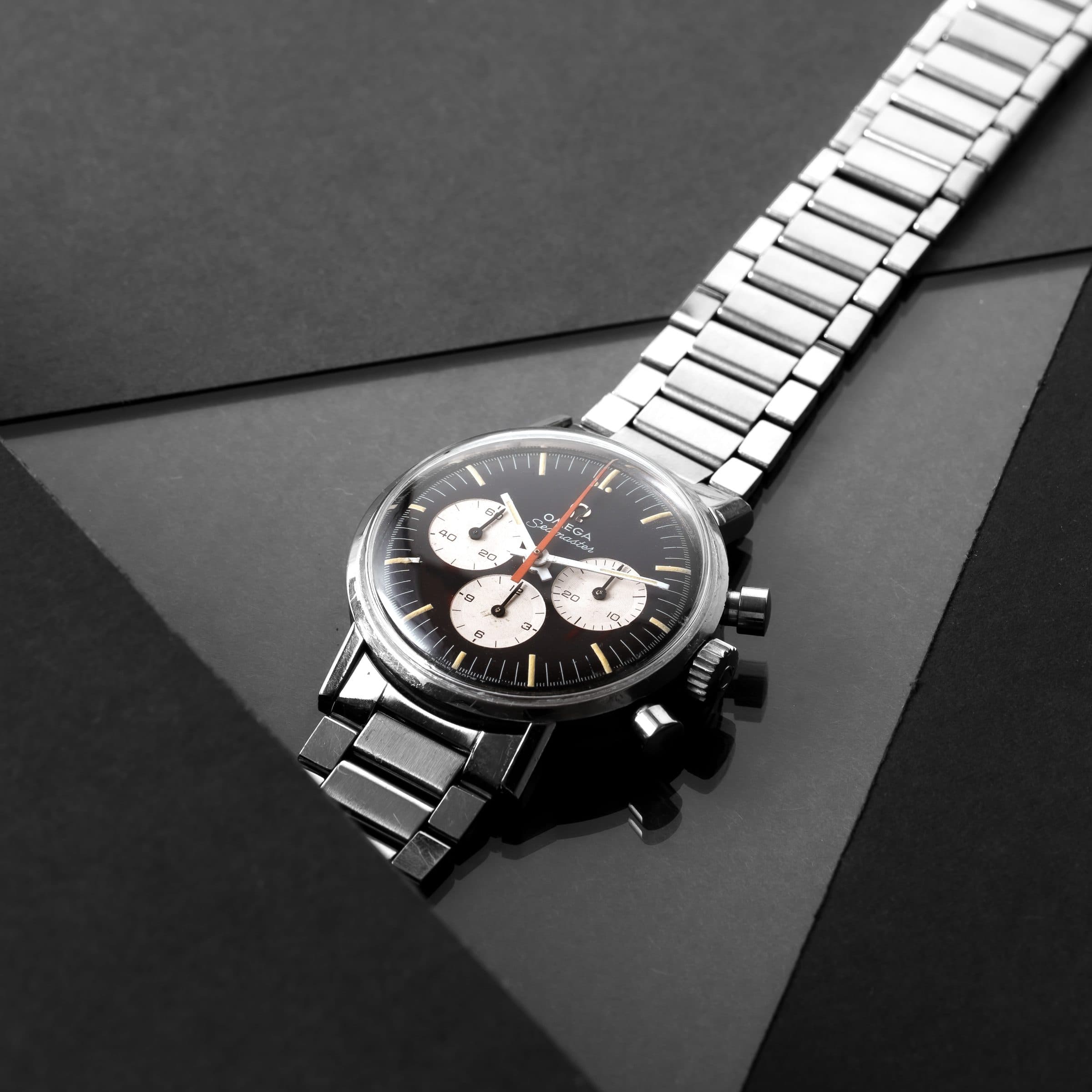 Steel chronograph with a black dial and white sub-dials on a dark stone surface